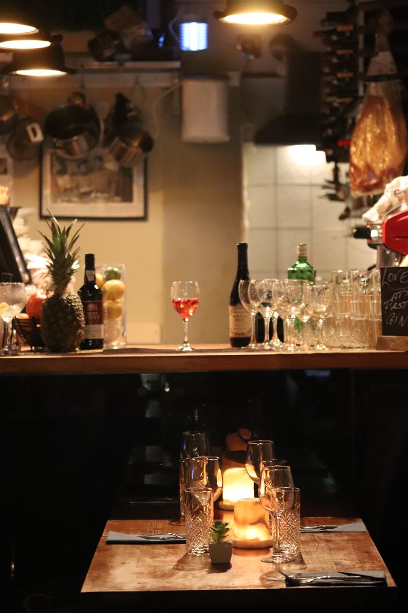 A candle-lit table in front of the bar, with pans hanging in the kitchen behind